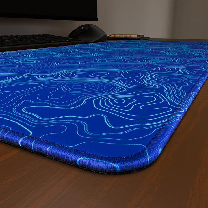 Close-up angled shot highlighting the durable stitched edges of a 90x40CM / 35x15.7in large mouse pad / desk mat with the 'Blue Topographic' design, inspired by blue minimalist topographic art. The reinforced stitching prevents fraying, ensuring long-lasting durability and a consistently clean aesthetic.
