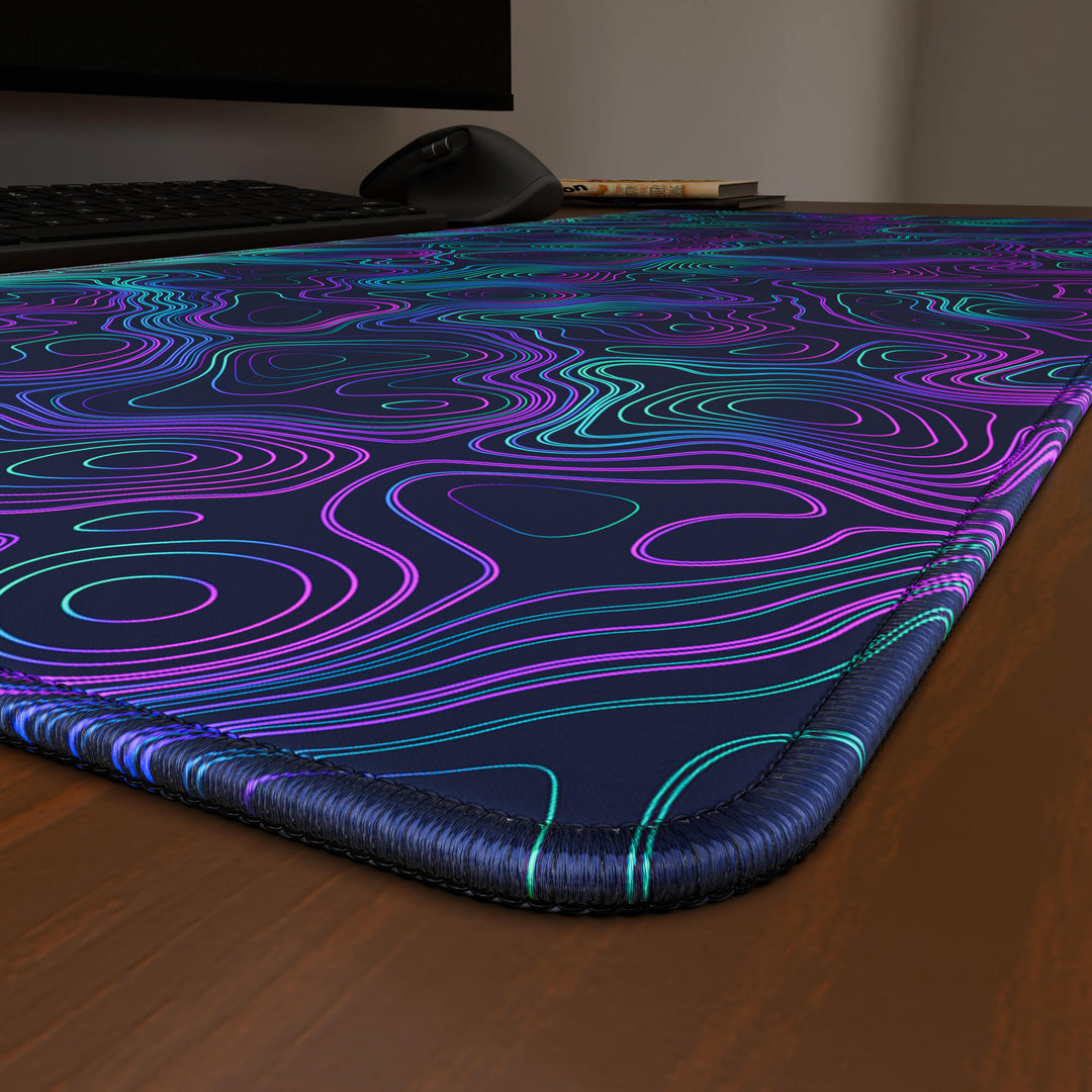 Close-up angled shot highlighting the durable stitched edges of a 90x40CM / 35x15.7in large mouse pad / desk mat with the 'Neon Topographic' design, inspired by vibrant neon topographic art. The reinforced stitching prevents fraying, ensuring long-lasting durability and a consistently clean aesthetic.