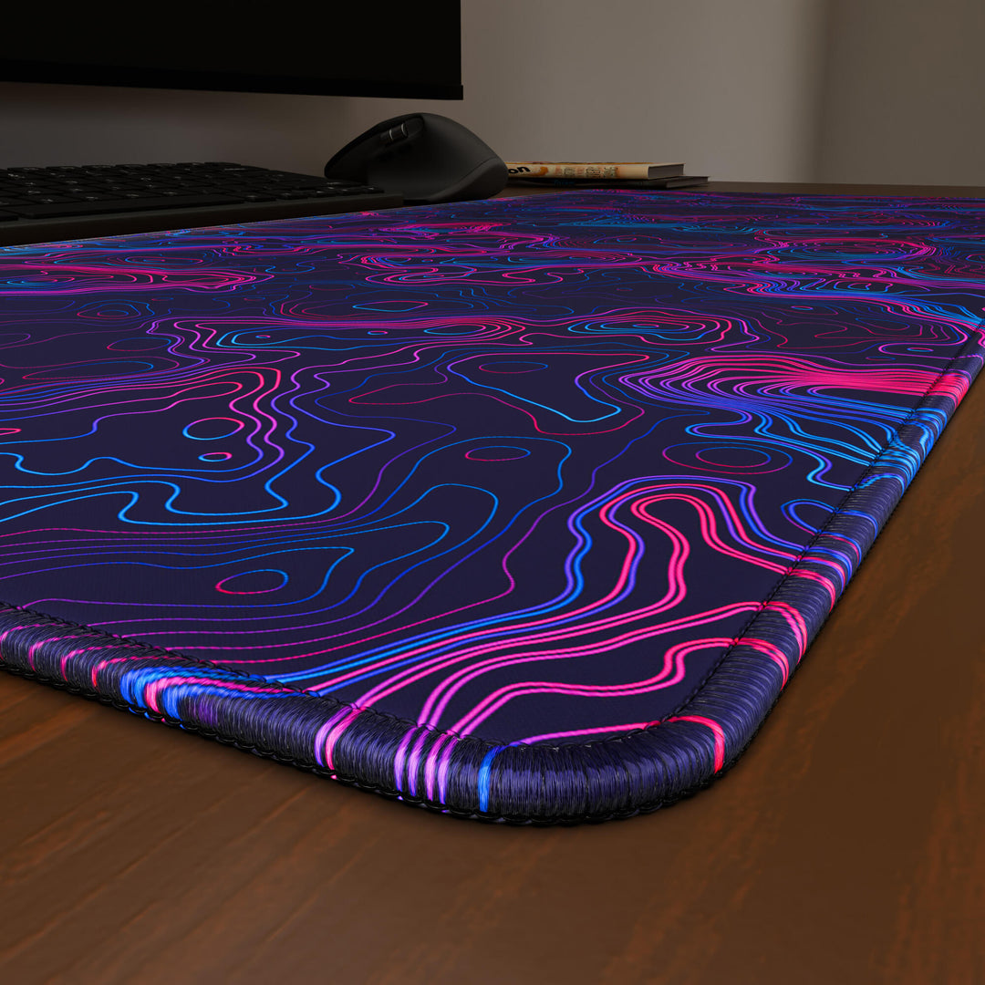 Close-up angled shot highlighting the durable stitched edges of a 90x40CM / 35x15.7in large mouse pad / desk mat with the 'Vaporwave Topographic' design, inspired by vibrant vaporwave and neon topographic art. The reinforced stitching prevents fraying, ensuring long-lasting durability and a consistently clean aesthetic.