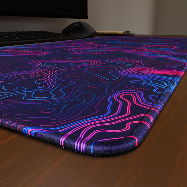Close-up angled shot highlighting the durable stitched edges of a 90x40CM / 35x15.7in large mouse pad / desk mat with the 'Vaporwave Topographic' design, inspired by vibrant vaporwave and neon topographic art. The reinforced stitching prevents fraying, ensuring long-lasting durability and a consistently clean aesthetic.